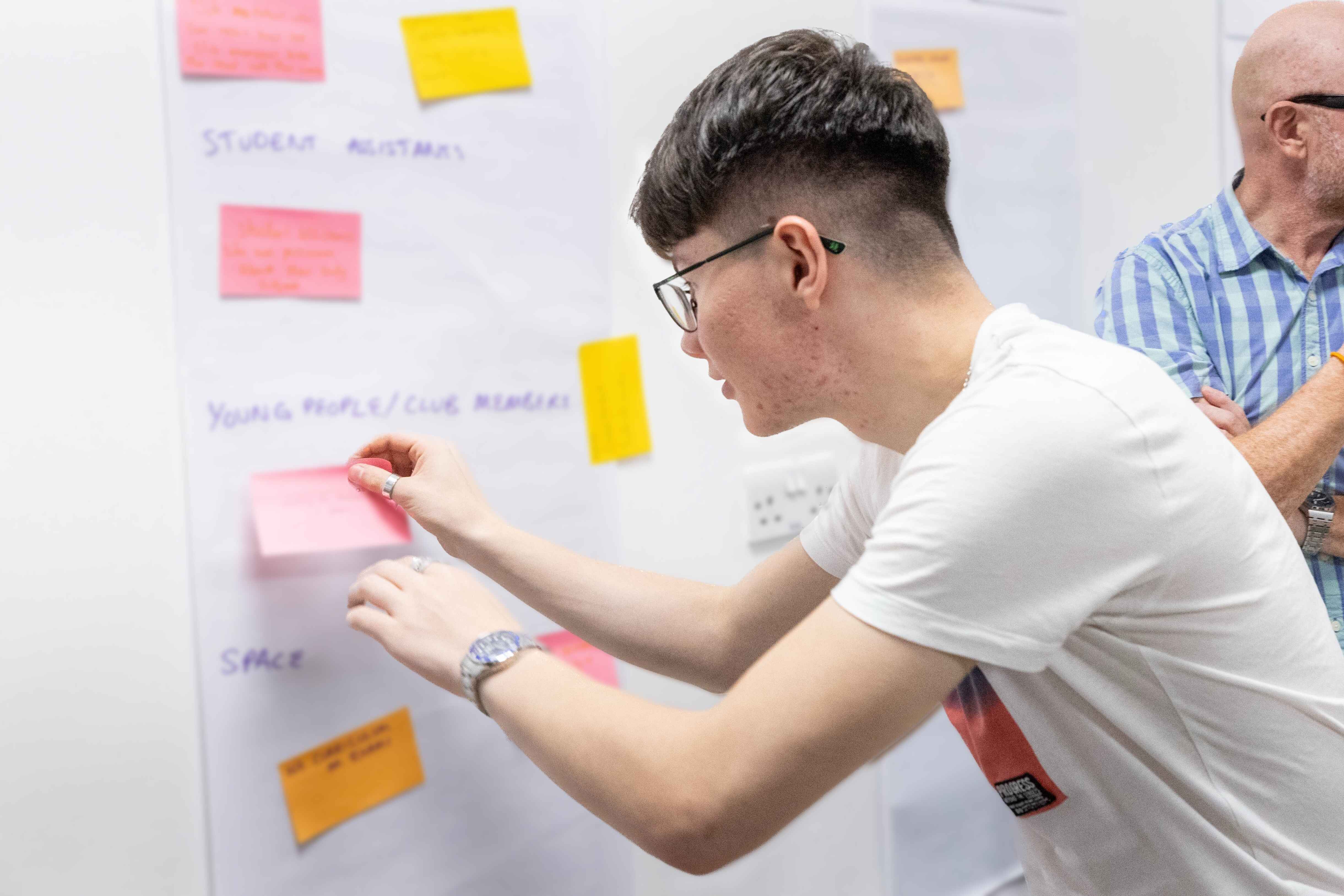 Liam Thompson placing post-it notes onto a whiteboard and brainstorming